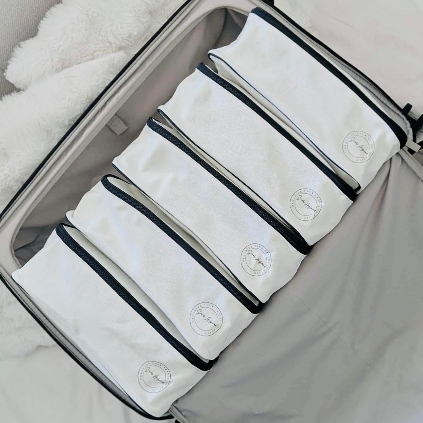 Set of 5 five cream cotton Canvas packing cubes with black trim in an open suitcase.