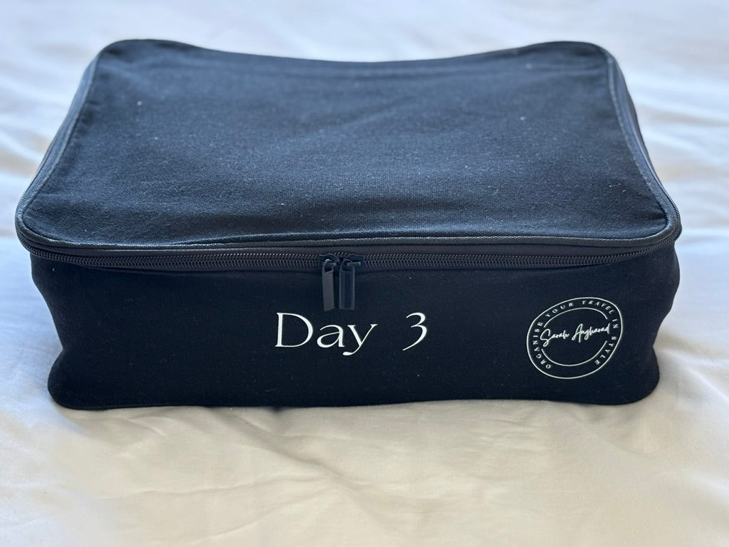 Black travel cube labeled 'Day 3' on a white bed sheet