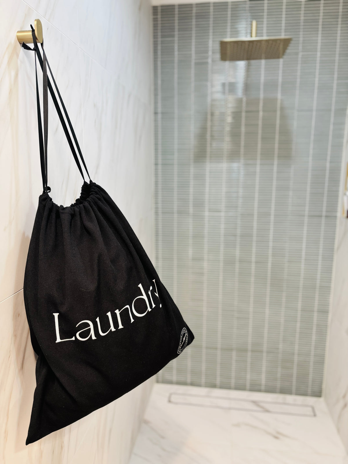 Black drawstring bag with 'Laundry' logo hanging on a hook in a bathroom.