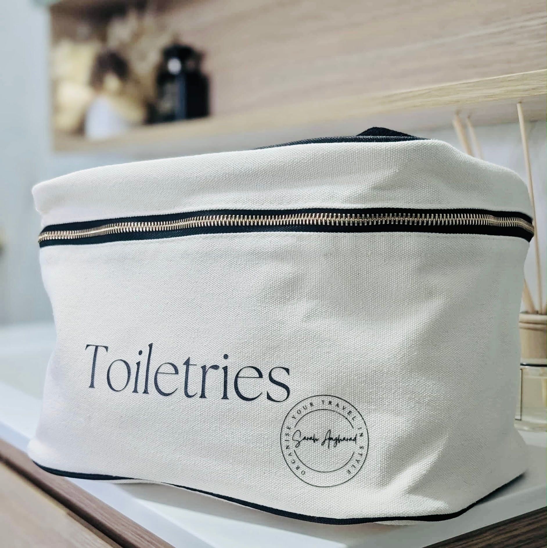 Cream toiletries bag with 'Toiletries' text and a logo on a blurred background