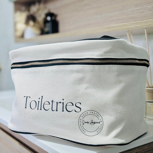 Cream toiletries bag with 'Toiletries' text and a logo on a blurred background