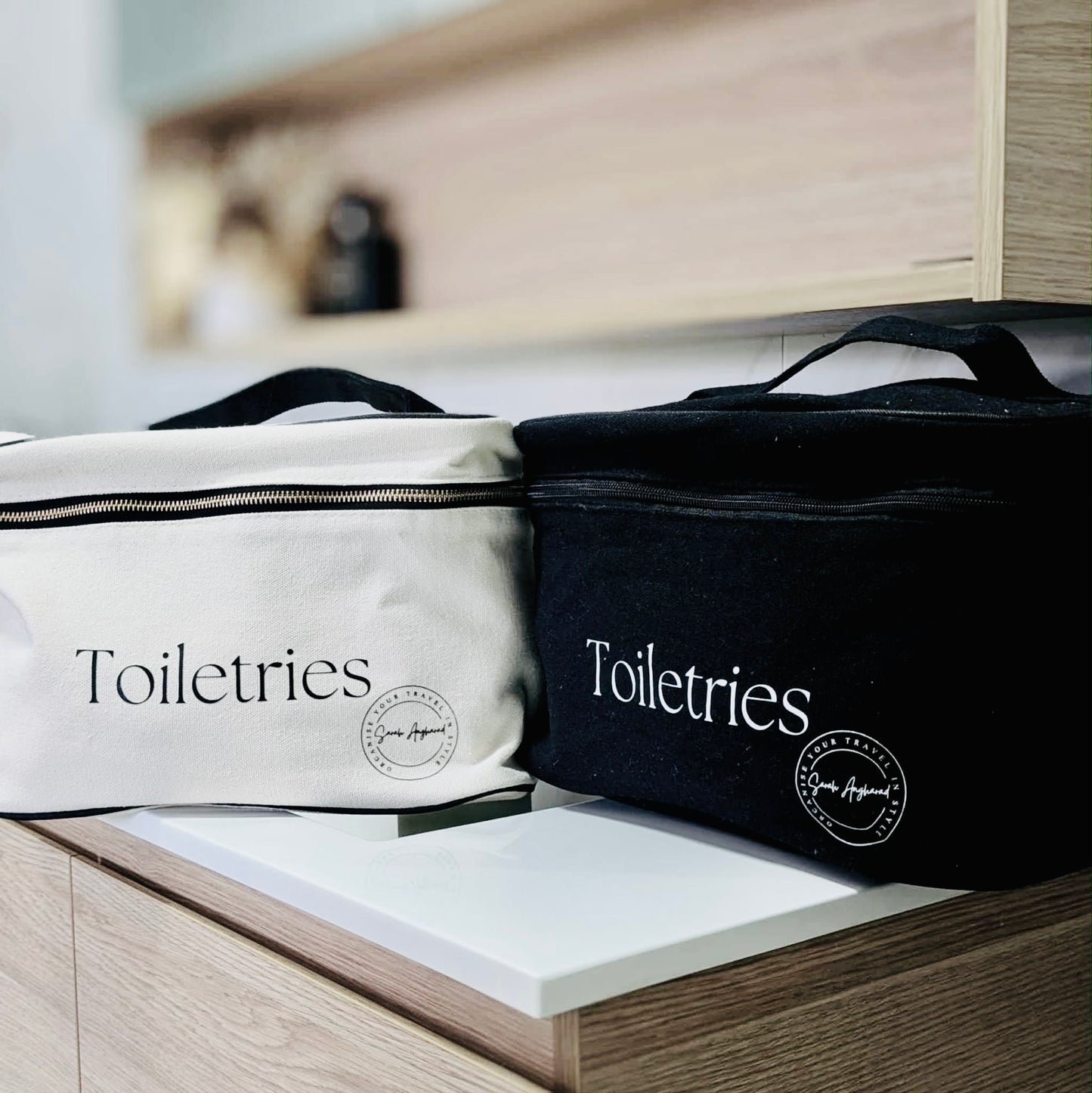 Two extra large toiletry bags, one in Black and one in cream with stylish branding positioned in a bathroomscene