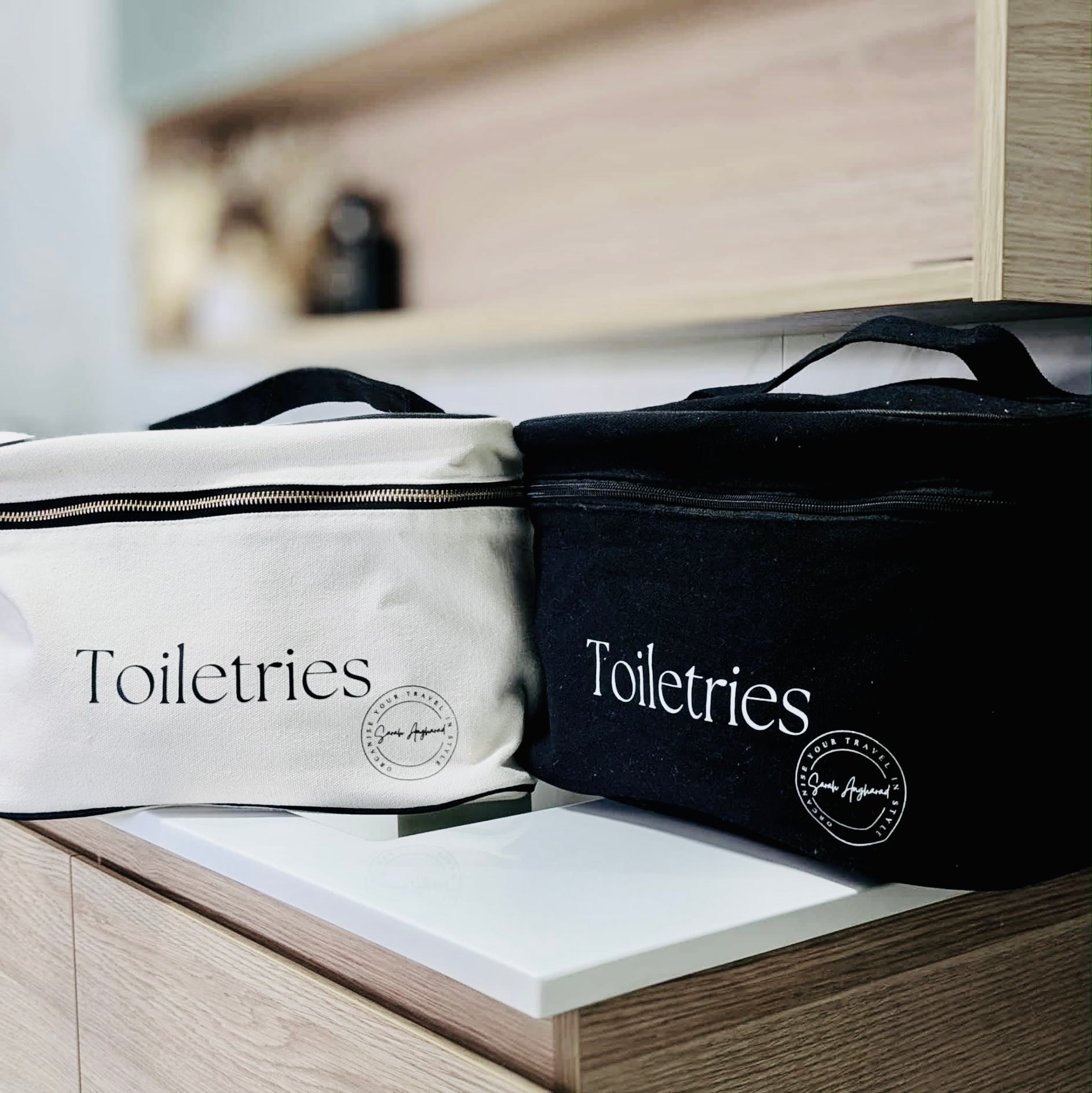 Two extra large toiletry bags, one in Black and one in cream with stylish branding positioned in a bathroomscene