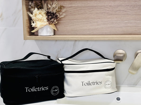 Two toiletry bags, one black and one white, on a bathroom counter with decorative elements.