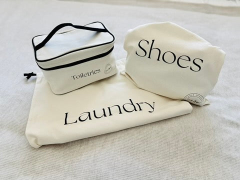 Three cream labeled bags for toiletries, shoes, and laundry on a light surface.